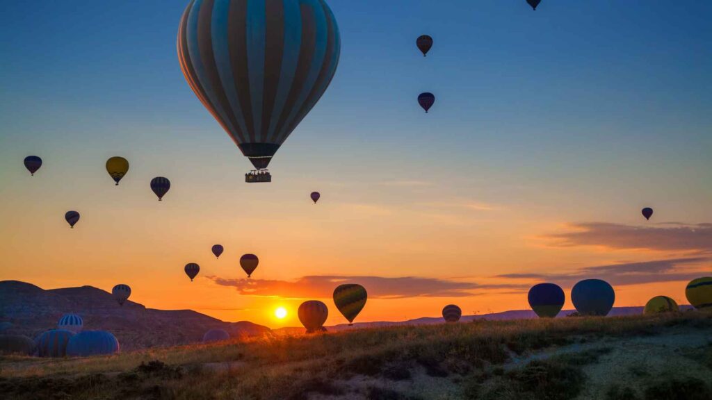 A photo of twenty hot air balloons floating into the sunset Valhalla Travel